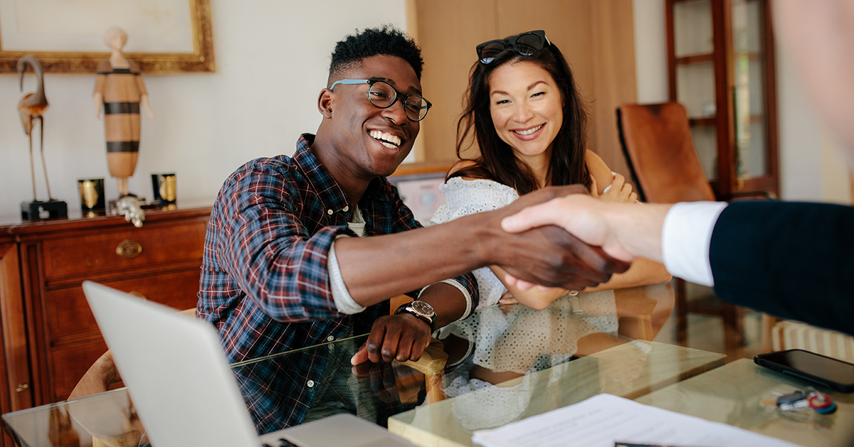 first-time home buyers shaking hands with agent in an office