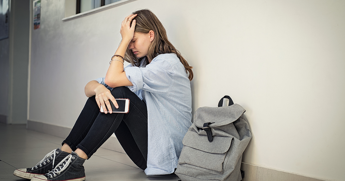 Teen girl sitting on the ground upset with phone and backpack