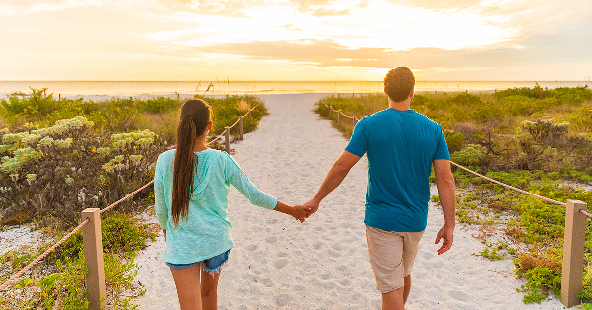 Couple holding hands while walking toward the beach at sunset in South Florida, representing an affordable Valentine’s date idea.