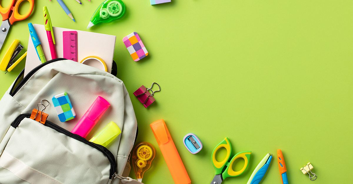 Open backpack with colorful school supplies scattered on a bright green background